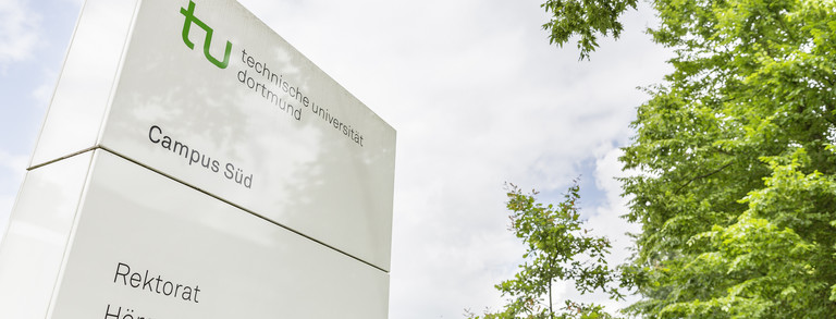 A white information board of Campus South stands next to green trees.
